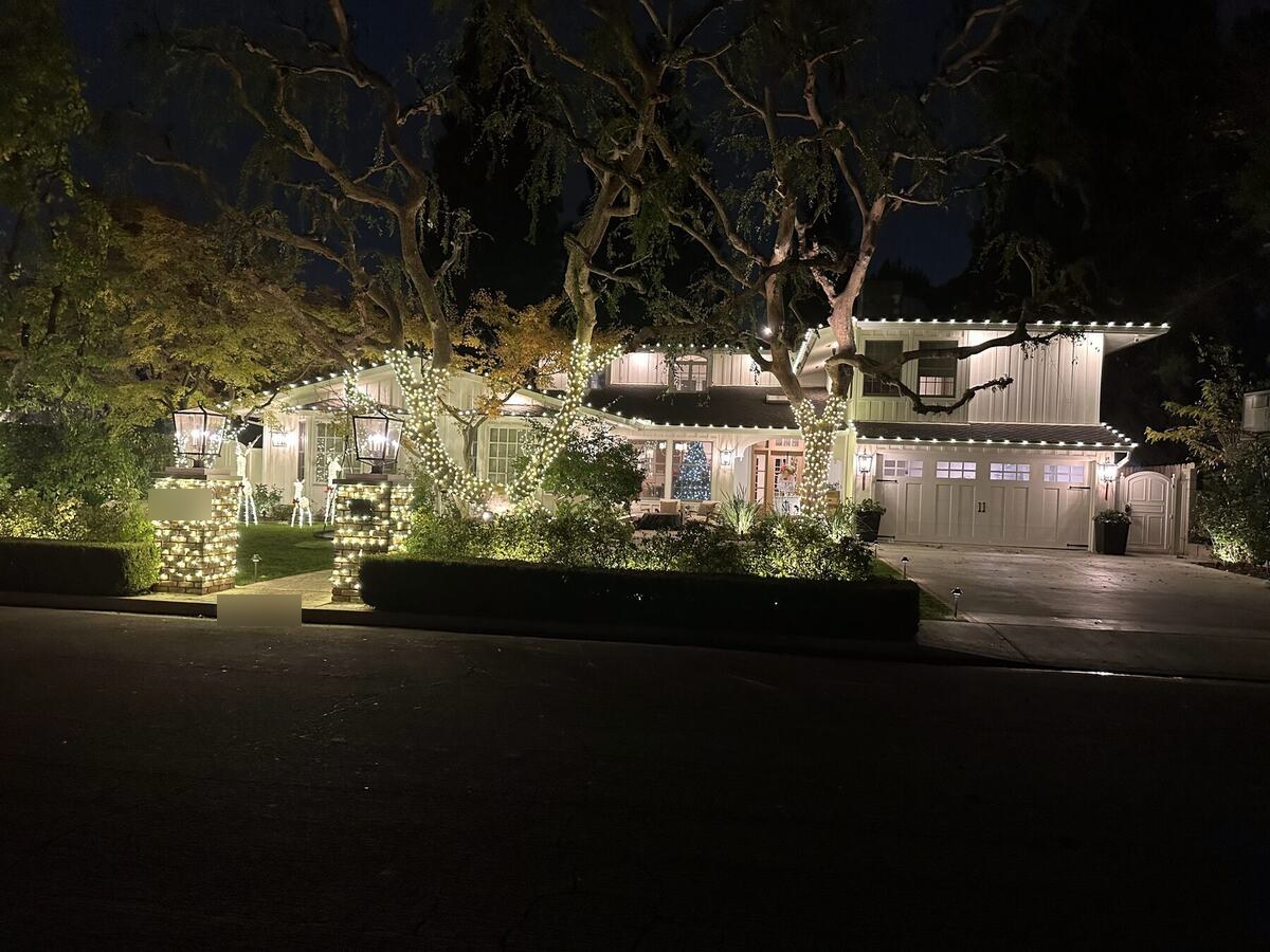 White board and batten Bakersfield home with warm white roofline lighting, lit garland on the entry columns and a wrapped oak tree
