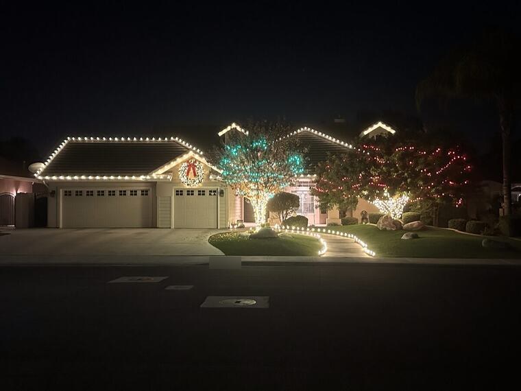 Bakersfield home with warm white roofline lights, a lit wreath over the entry and green and red wrapped trees