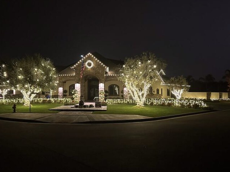 Large Bakersfield estate with warm white roofline lighting and rows of wrapped trees along the drive