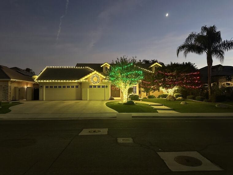 Bakersfield home at twilight with warm white roofline lights and color wrapped trees under a rising moon